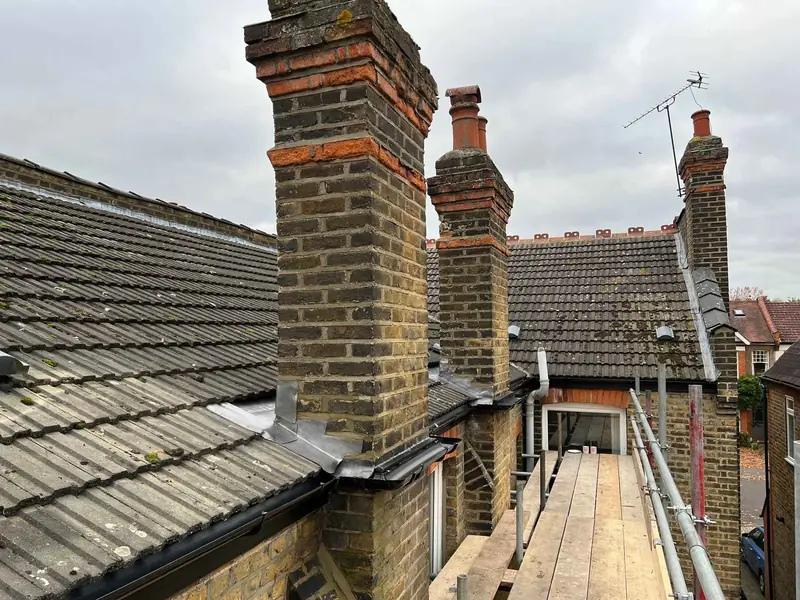 Three brick chimney stacks rising from a tiled roof, with lead at their base