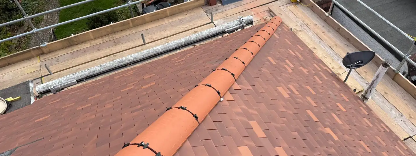 Terracotta ridge running up a newly tiled bungalow roof, with the scaffold alongside