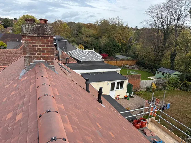Freshly laid roof tiles meeting a brick chimney on a re-roof