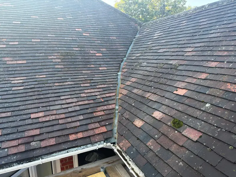 Worn plain tiles on a hipped bungalow roof, with moss in the valley