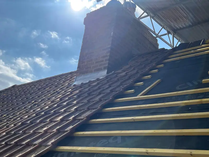 Re-roof in progress beside a chimney: new battens on black membrane
