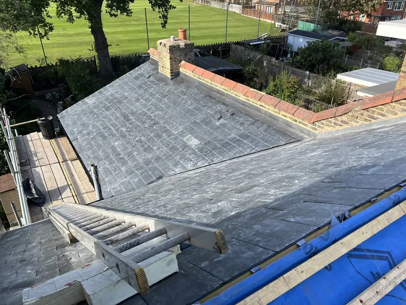 Slate roof being repaired from a scaffold, with a ladder on the roof