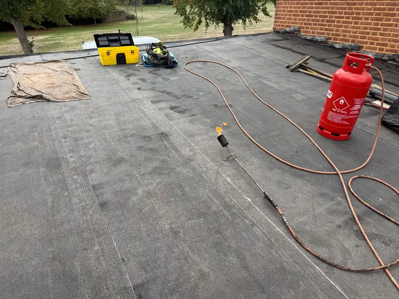 Flat roof part-covered in new felt, with a gas bottle and torch on it
